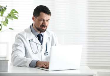 Male doctor working with laptop at table in office