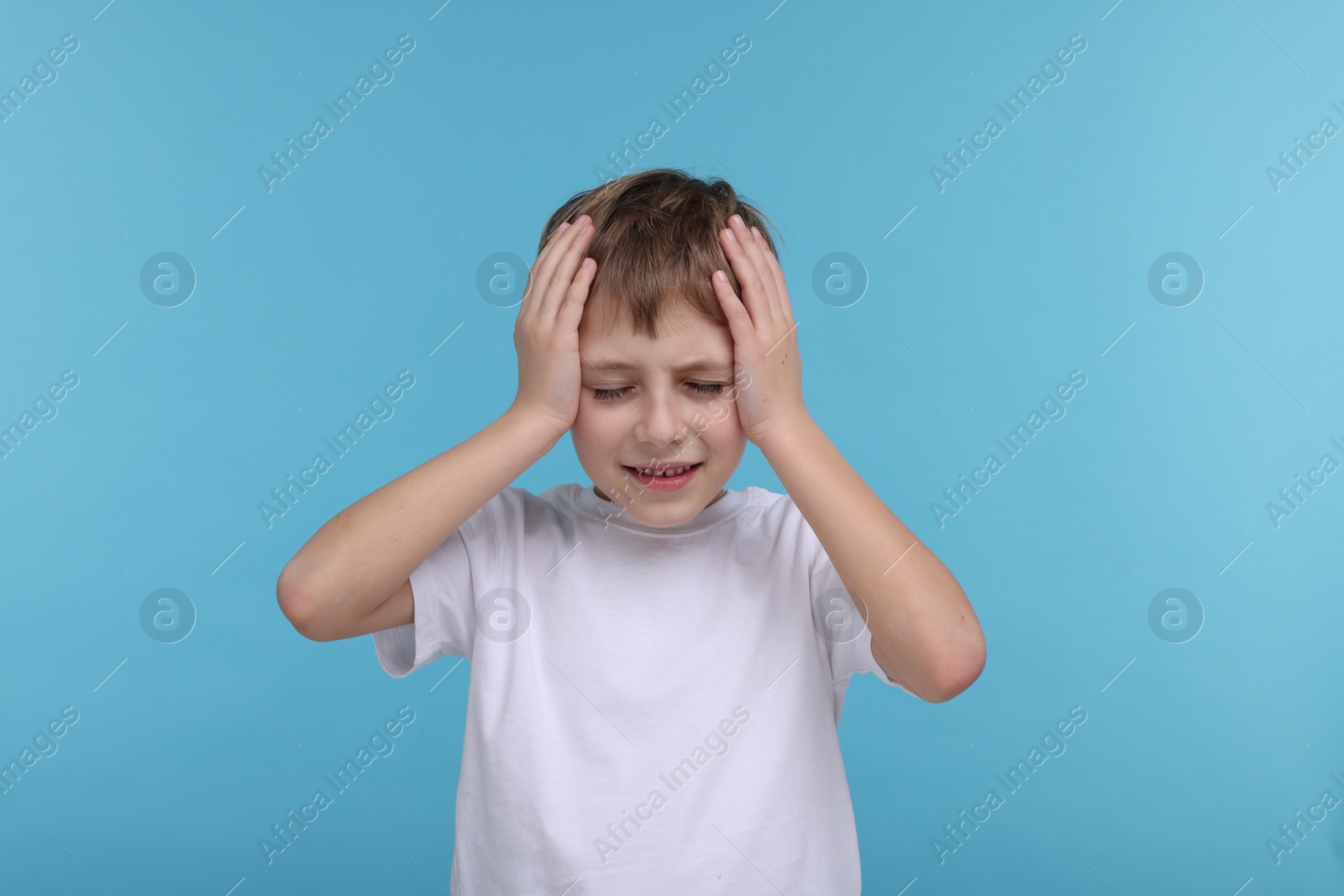 Photo of Little boy suffering from headache on light blue background