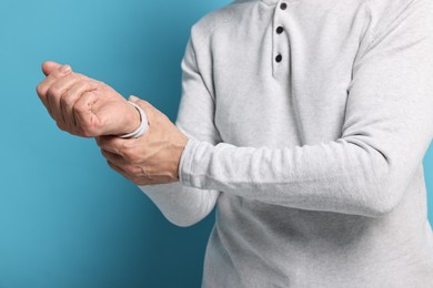 Photo of Arthritis symptoms. Man suffering from pain in wrist on light blue background, closeup