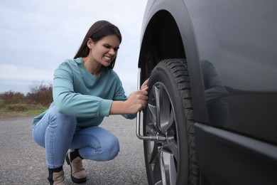 Photo of Young woman changing tire of car outdoors