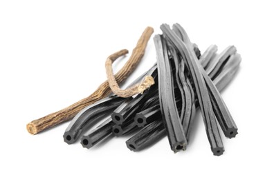Tasty black candies and dried sticks of liquorice root on white background