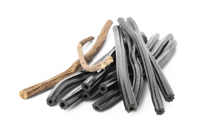 Photo of Tasty black candies and dried sticks of liquorice root on white background