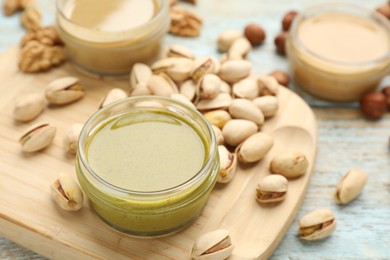 Different types of delicious nut butters and ingredients on light blue wooden table, closeup