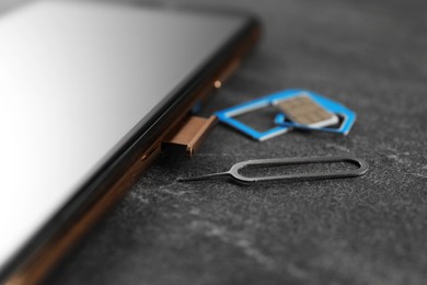 SIM card, mobile phone and ejector tool on grey table, closeup