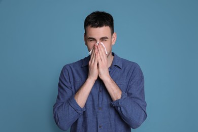 Photo of Young man blowing nose in tissue on blue background. Cold symptoms