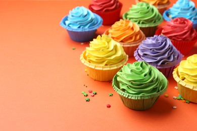 Photo of Delicious bright cupcakes and sprinkles on coral background. Space for text