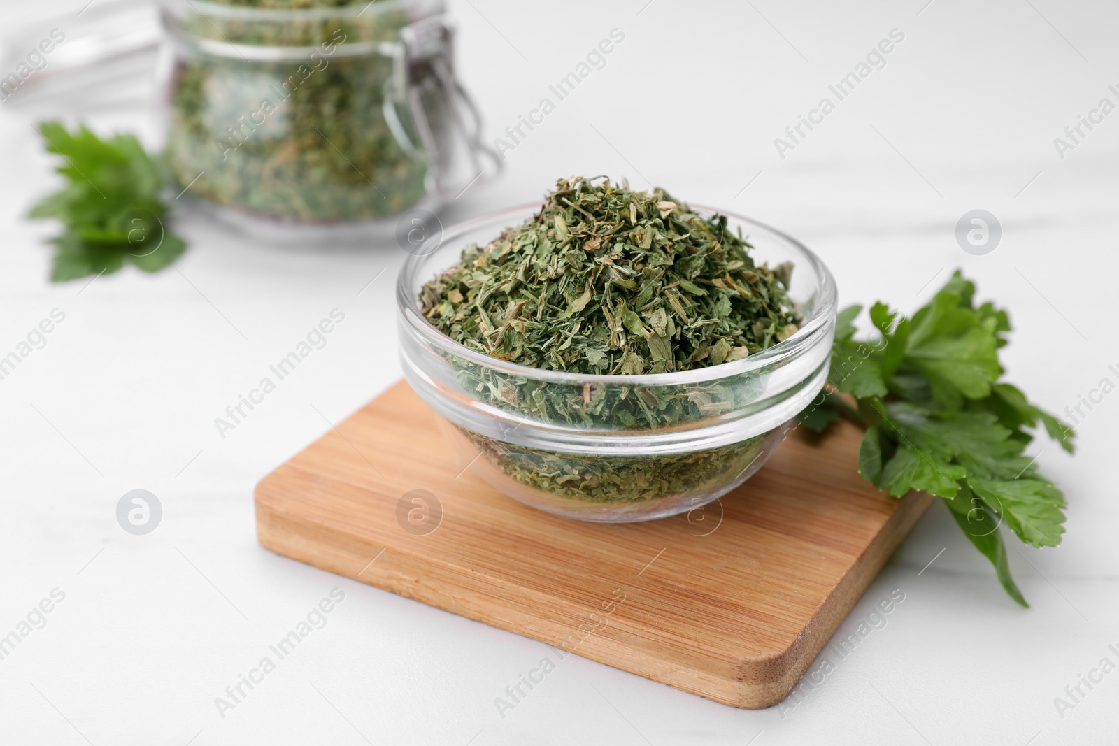 Photo of Dried aromatic parsley in glass bowl and fresh leaves on white table