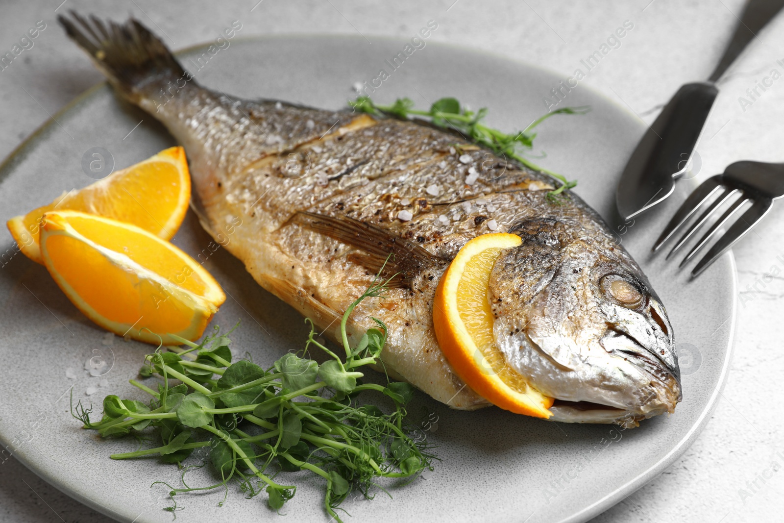 Photo of Seafood. Delicious baked fish served with orange and microgreens on light table, closeup