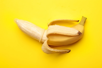 Banana with condom on yellow background, top view. Safe sex