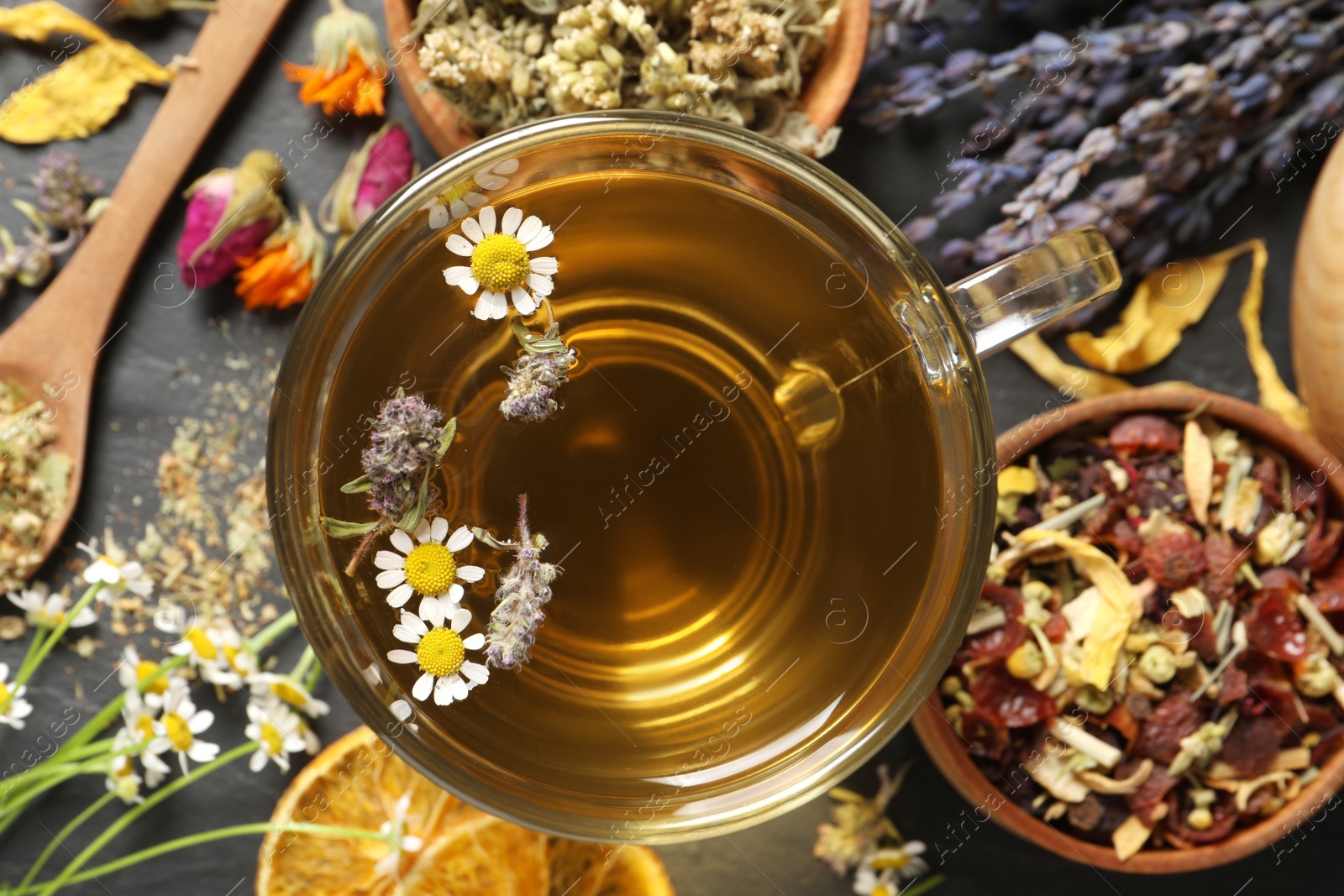 Photo of Glass cup of aromatic freshly brewed tea near different dry herbs on black table, flat lay