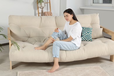 Photo of Young woman rubbing sore leg on sofa at home