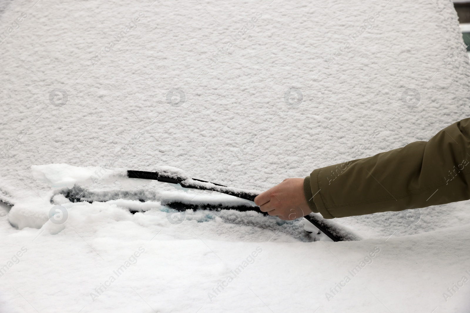 Photo of Woman cleaning car wiper blade covered with snow, closeup