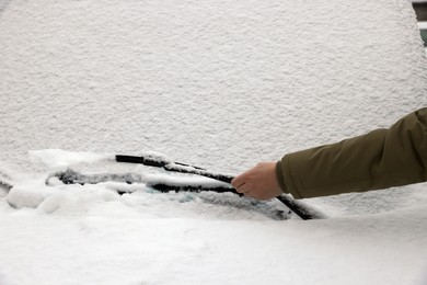 Photo of Woman cleaning car wiper blade covered with snow, closeup