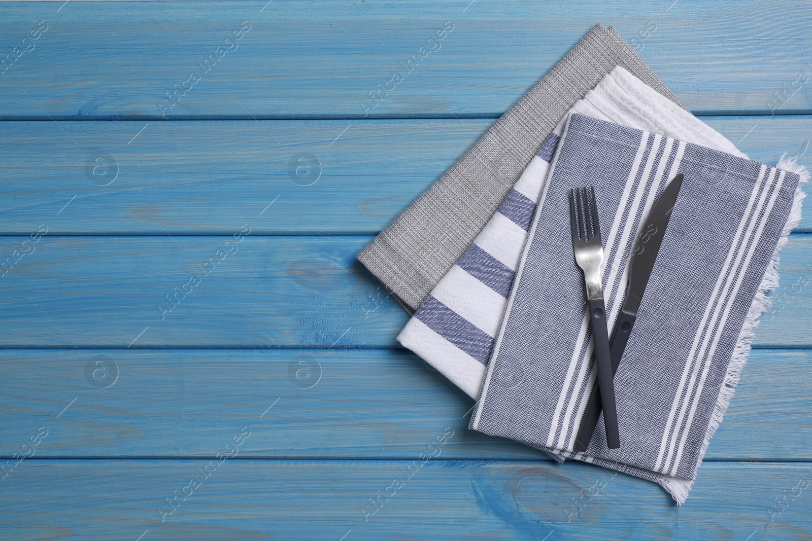 Photo of Different kitchen towels with cutlery on blue wooden table. Space for text