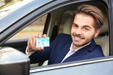 Photo of Young man holding driving license in car