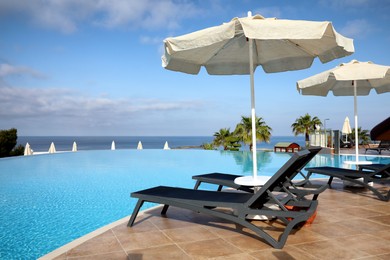 Photo of Chaise longues and beach parasols near infinity pool at resort