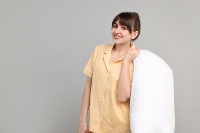 Photo of Happy woman in pyjama holding pillow on grey background, space for text