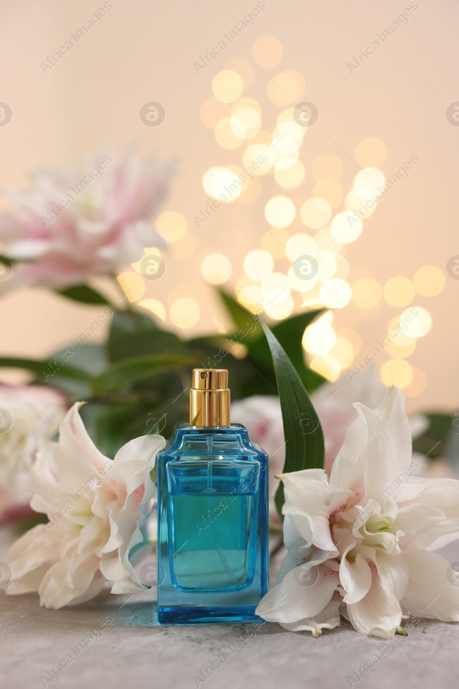 Photo of Bottle of perfume and beautiful lily flowers on table against beige background with blurred lights, closeup