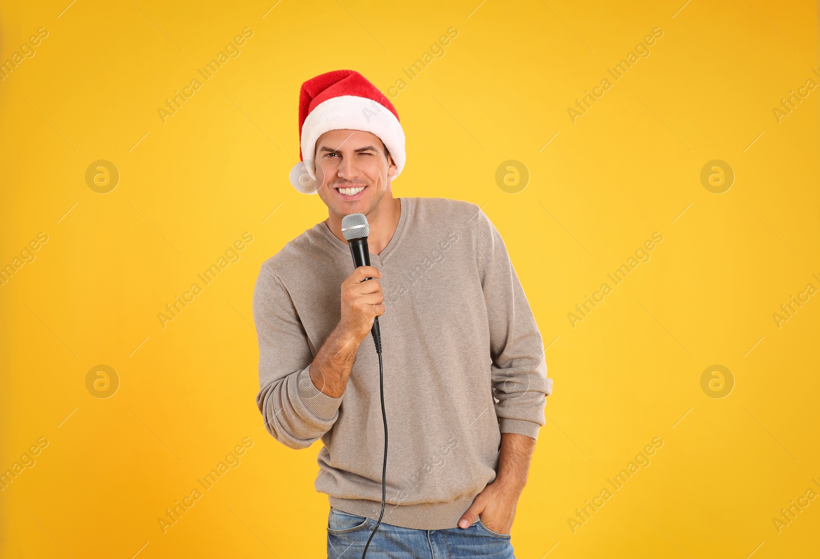 Photo of Happy man in Santa Claus hat with microphone on yellow background. Christmas music