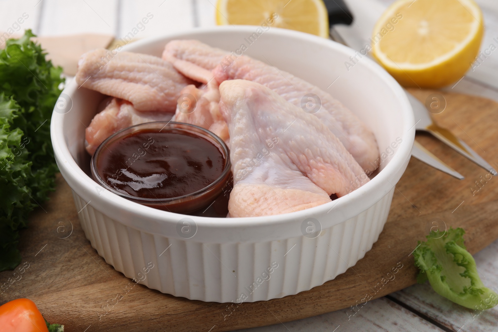 Photo of Fresh marinade, raw chicken wings and other products on rustic wooden table, closeup