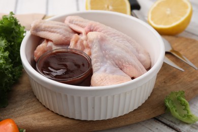 Fresh marinade, raw chicken wings and other products on rustic wooden table, closeup