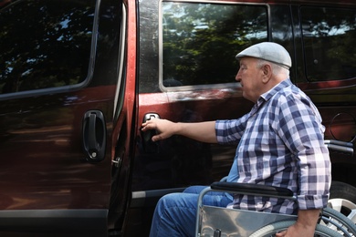 Senior man in wheelchair opening door of his van outdoors