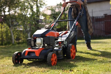 Photo of Man cutting green grass with lawn mower in garden, selective focus