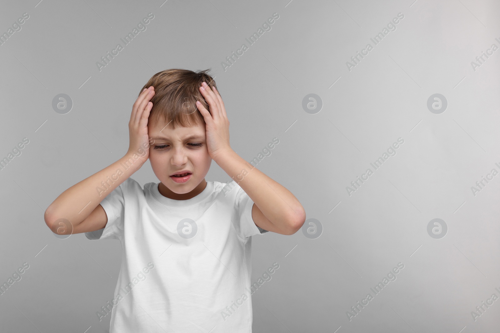 Photo of Little boy suffering from headache on grey background, space for text