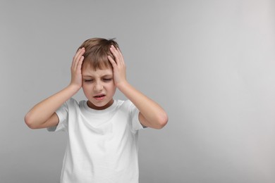 Little boy suffering from headache on grey background, space for text