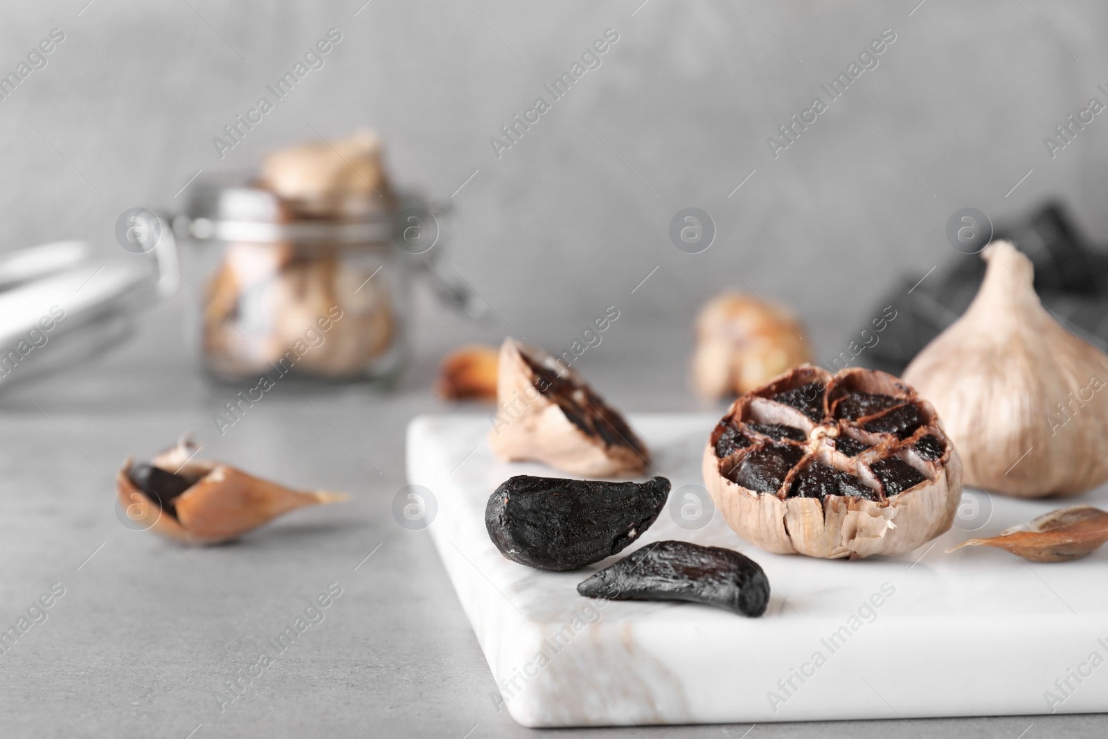 Photo of Marble board with black garlic on grey table. Space for text