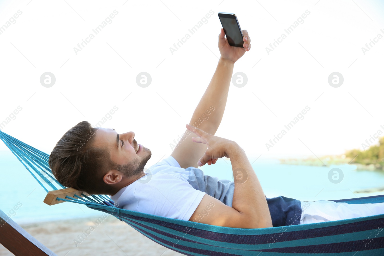 Photo of Young man taking selfie in hammock at seaside