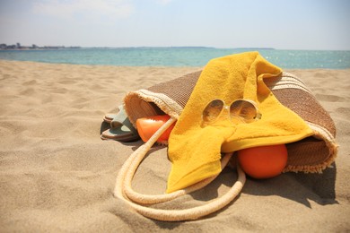 Beach bag, sunglasses and other accessories on sand near sea. Space for text