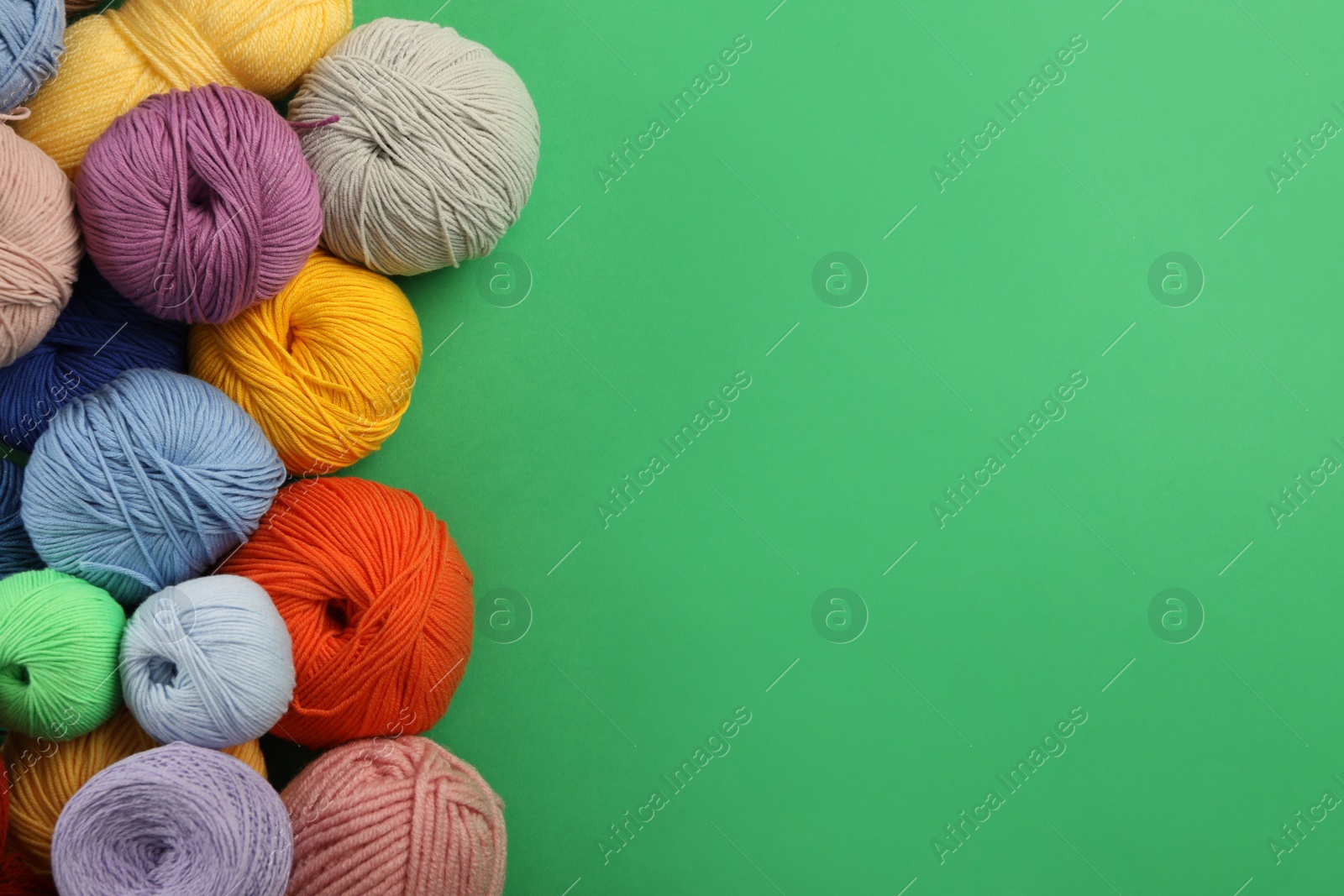 Photo of Soft woolen yarns on green background, flat lay. Space for text