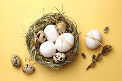 Nest with different eggs and fluffy willow branch on yellow background, flat lay. Happy Easter