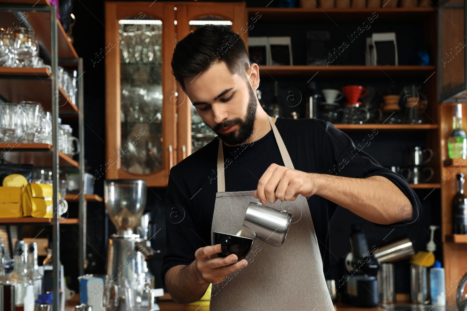 Photo of Portrait of barista pouring milk into cup of coffee against bar shelves in cafe