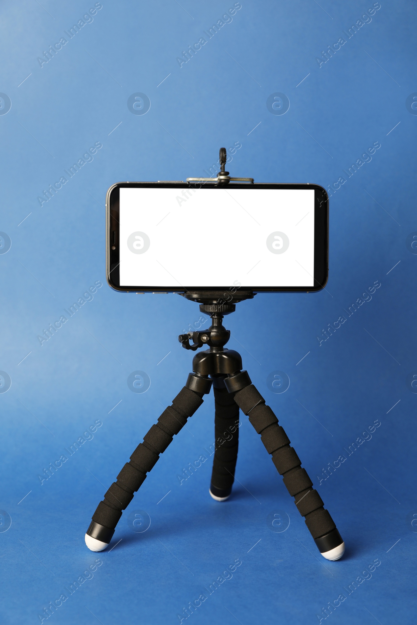 Photo of Modern tripod with smartphone on blue background