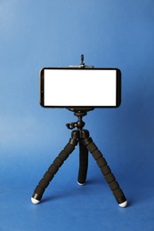 Modern tripod with smartphone on blue background