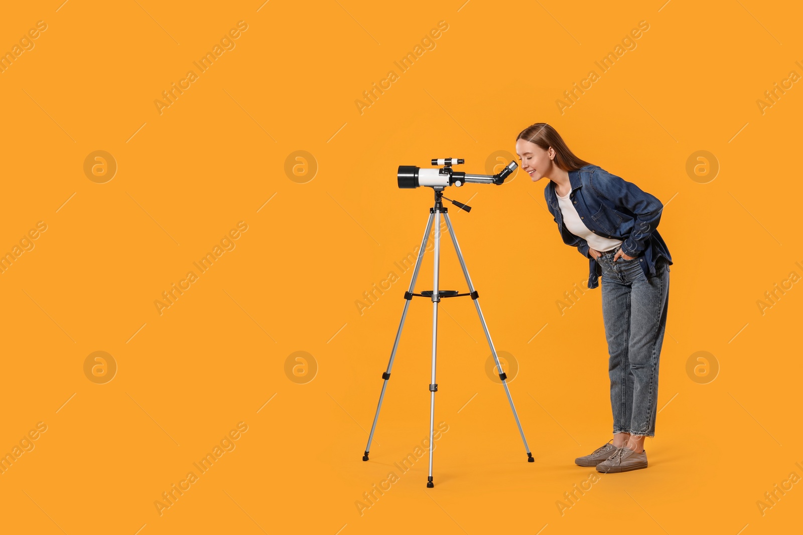 Photo of Young astronomer looking at stars through telescope on orange background, space for text