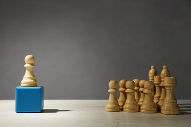 Photo of White chess piece standing out from others on wooden table against grey background