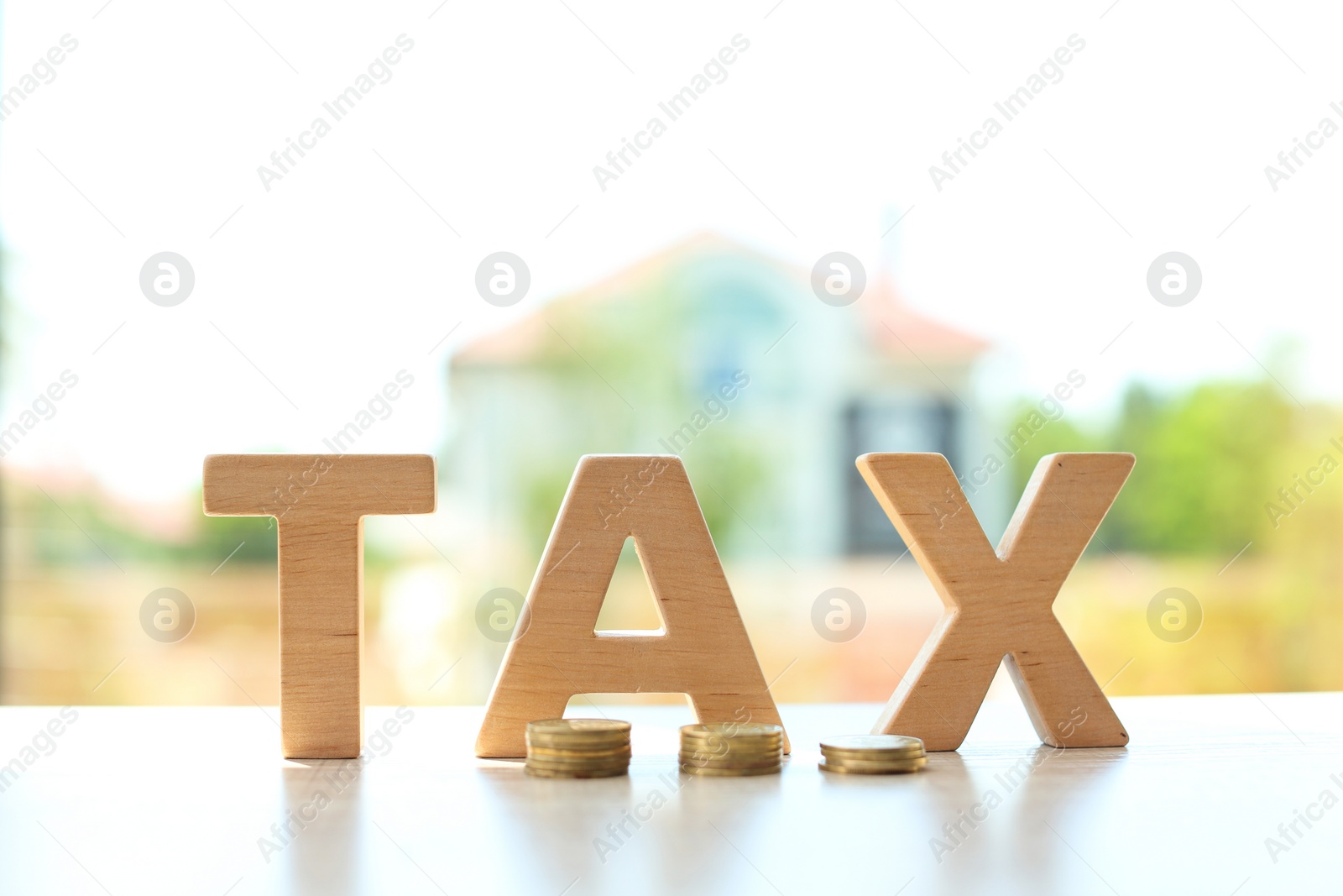Photo of Word TAX and coins on table against blurred background