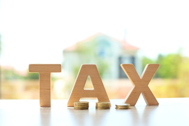 Word TAX and coins on table against blurred background