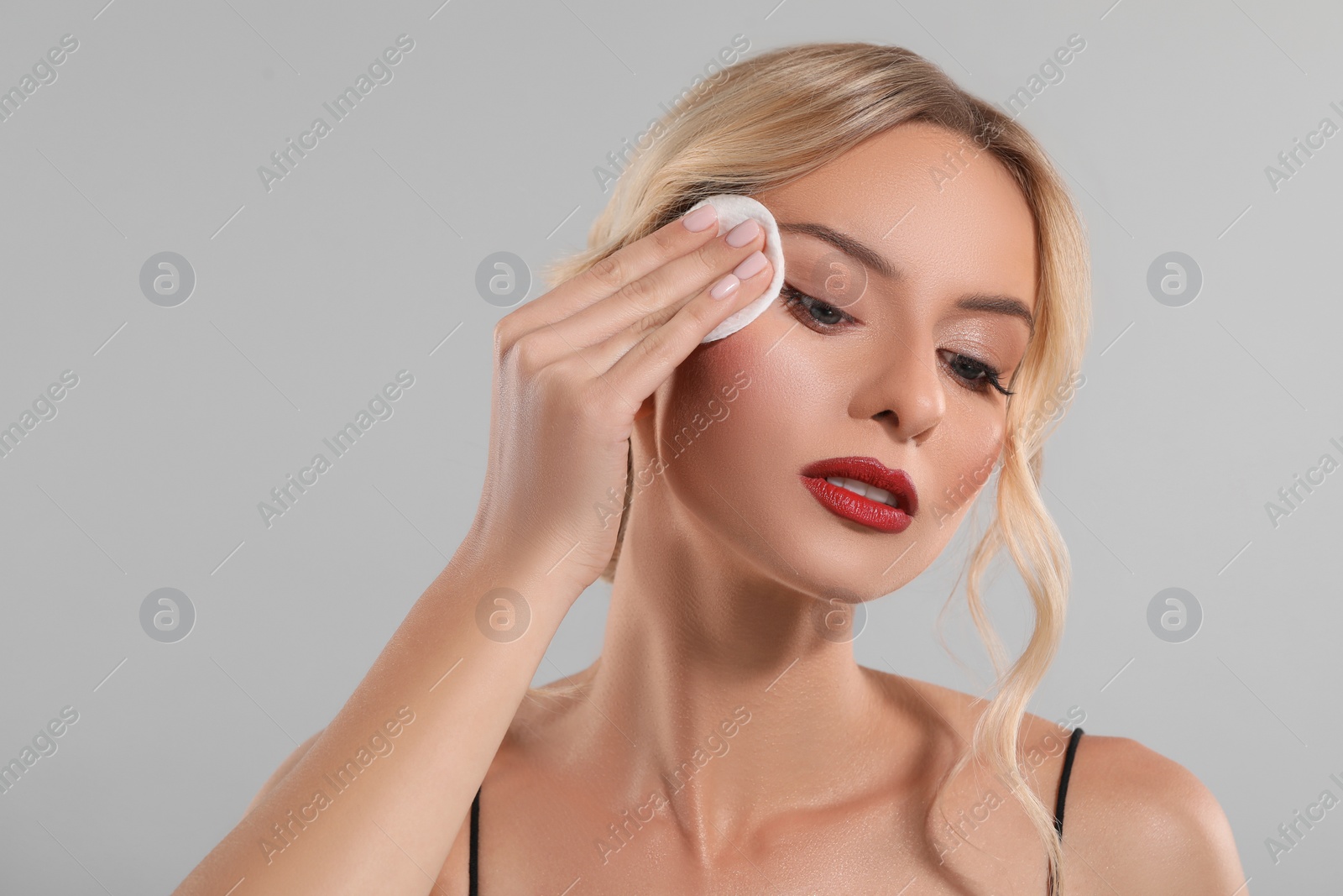 Photo of Beautiful woman removing makeup with cotton pad on light grey background