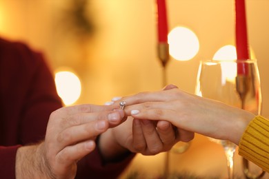 Making proposal. Man putting engagement ring on his girlfriend's finger at home on Christmas, closeup