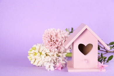 Photo of Stylish bird house and fresh hyacinths on violet background. Space for text