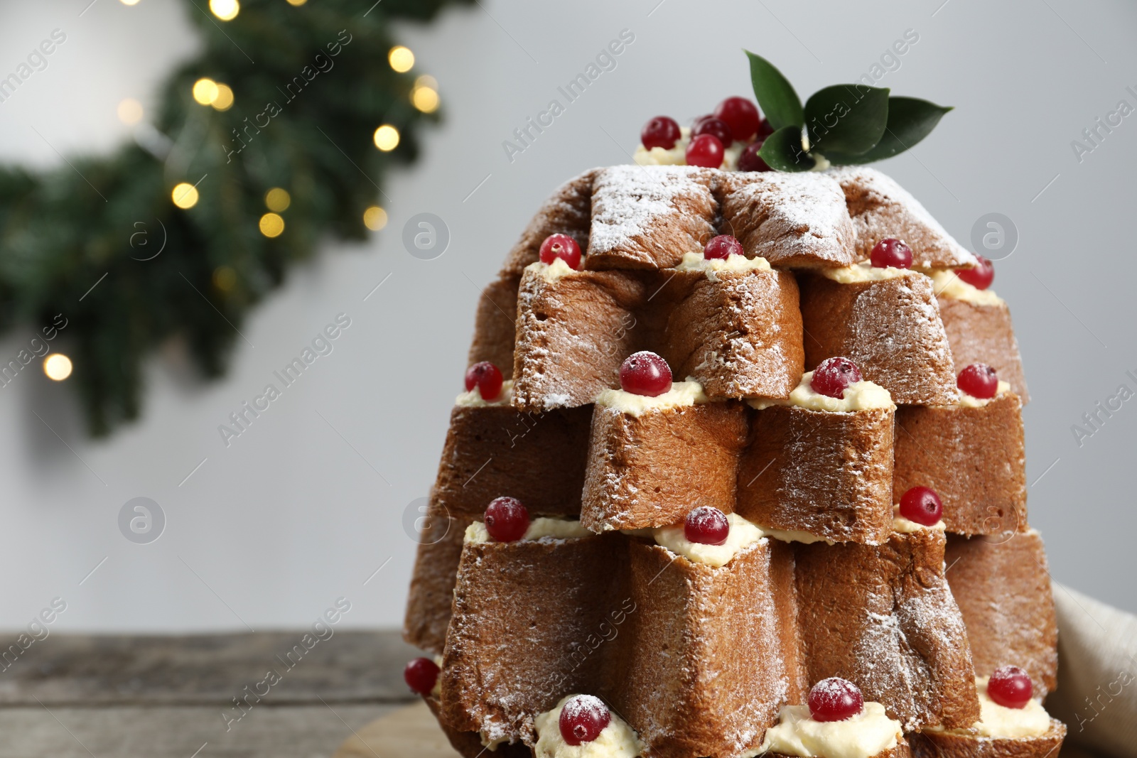 Photo of Delicious Pandoro Christmas tree cake with powdered sugar and berries near festive decor on wooden table, closeup. Space for text