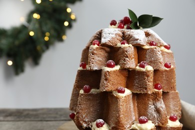 Delicious Pandoro Christmas tree cake with powdered sugar and berries near festive decor on wooden table, closeup. Space for text