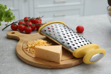 Wooden board with grater and cheese on grey table