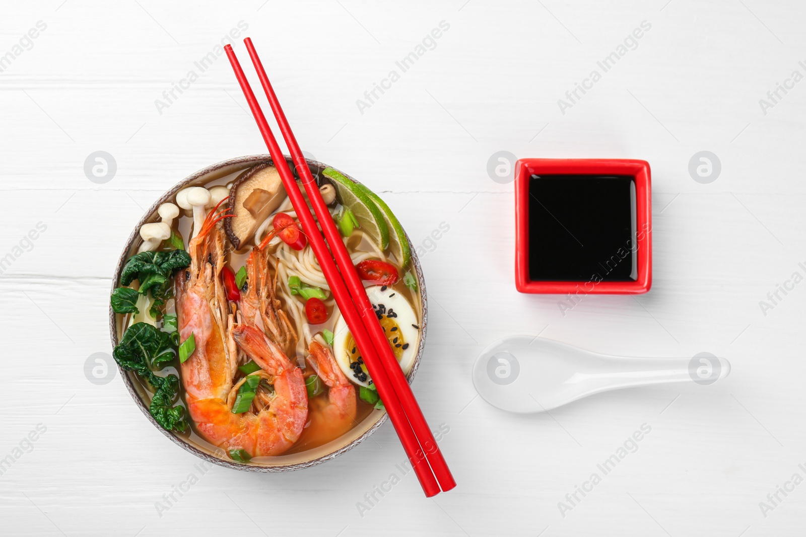 Photo of Delicious ramen with shrimps and egg in bowl served on white wooden table, flat lay. Noodle soup