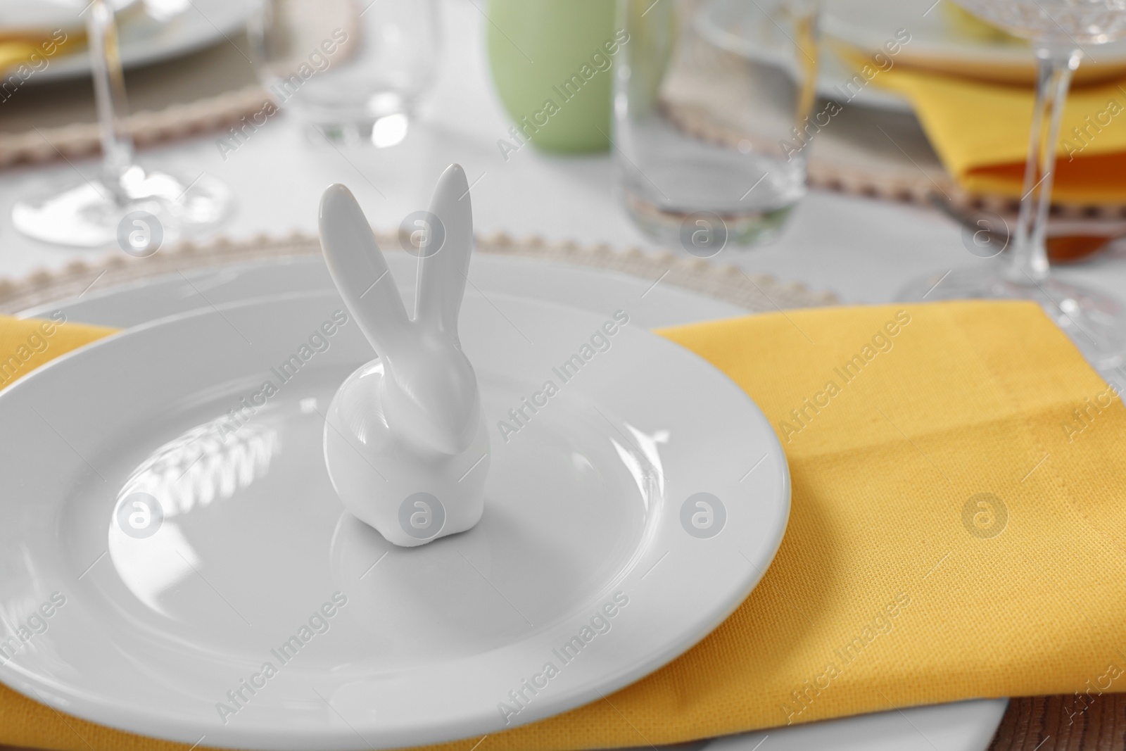 Photo of Festive table setting with cutlery, plate and bunny figure, closeup. Easter celebration