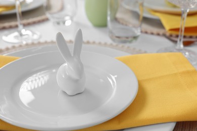 Festive table setting with cutlery, plate and bunny figure, closeup. Easter celebration